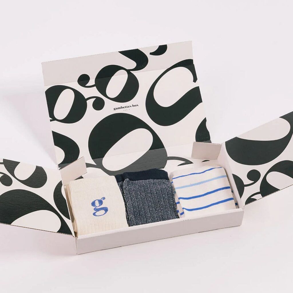 La nouvelle box de chaussettes par abonnement de Gambettes Box, avec boîte ouverte laissant entrevoir les chaussettes