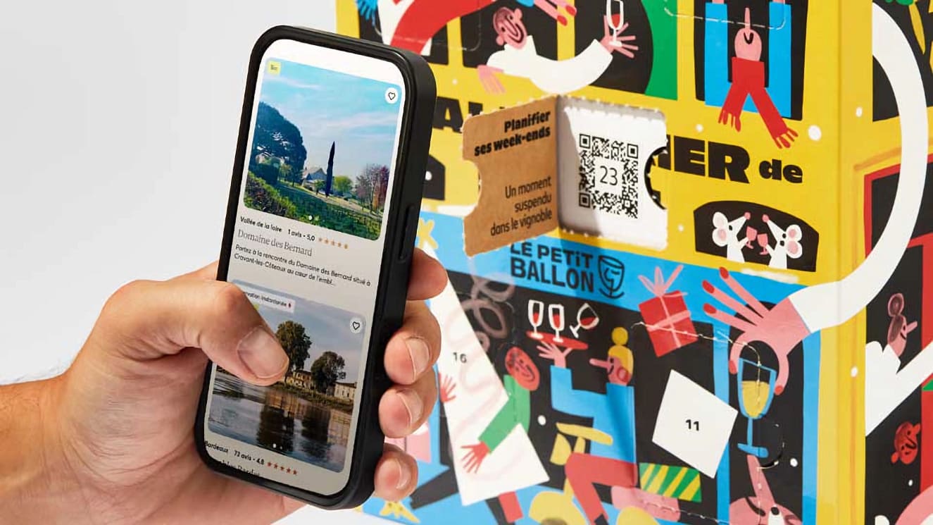 Main tenant un smartphone affichant une fiche de domaine viticole, face à une case ouverte du calendrier avec un QR code.