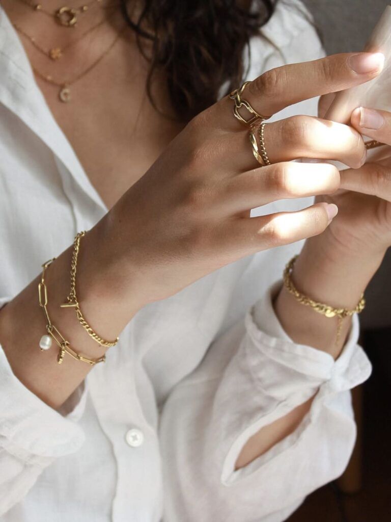 bracelets et bagues dorés portés femme avec accumulation de bijoux tendance en acier inoxydable