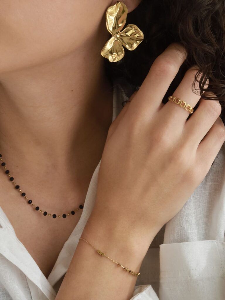 zoom sur bijoux femme portés avec boucles d’oreilles dorées, bague et bracelet tendance