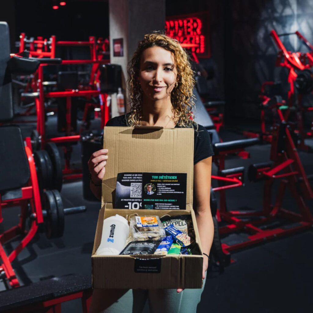 Myriam Belgacem fondatrice de MYR PROT BOX tenant une box fitness protéinée dans une salle de musculation