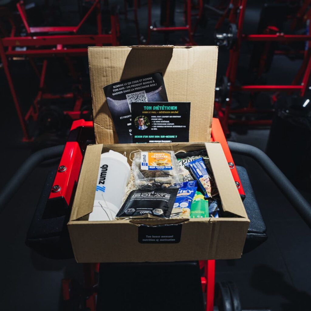 box fitness lifestyle avec shaker, barres et compléments dans ambiance salle de musculation