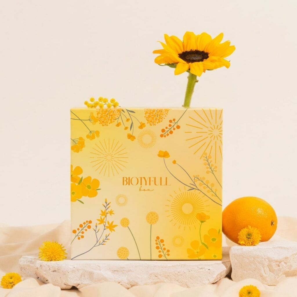 Design de la Biotyfull Box 100% Bronzage Éclatant avec motif floral jaune et ambiance estivale