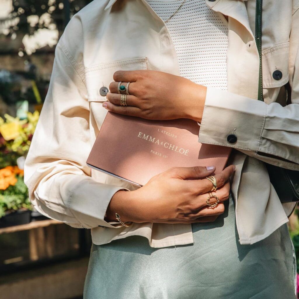 Gros plan sur une sélection de bagues et bracelets dorés portés avec un coffret de bijoux en arrière-plan