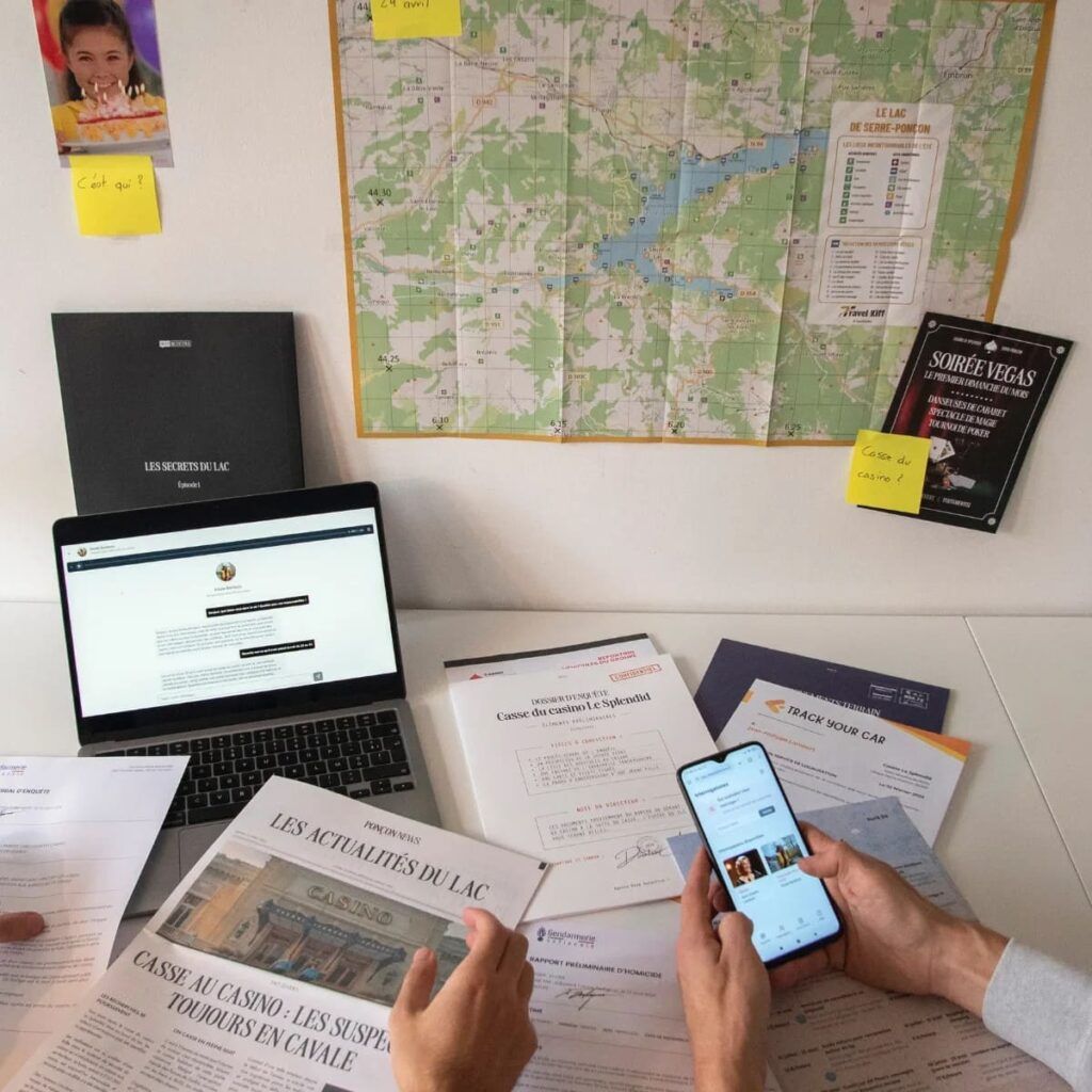 Joueurs examinant les documents et indices d’un jeu d’enquête avec smartphone et ordinateur