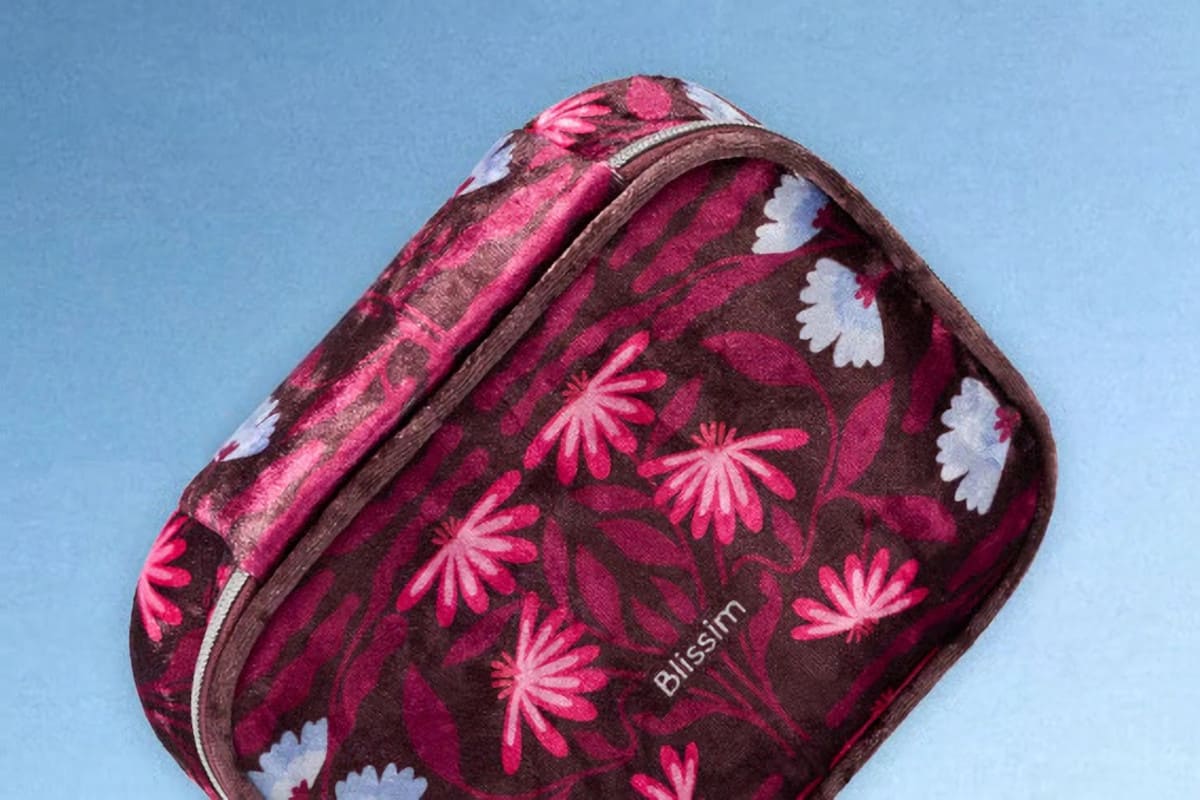 Design de la box Blissim de décembre 2026, une trousse zippée en tissu à l’aspect doux, ornée de fleurs roses et blanches sur fond bordeaux foncé