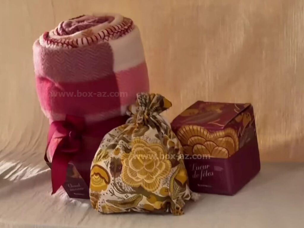 Premier spoiler de My Little Box novembre décembre 2026 avec un plaid rose, un pochon à motifs fleuris et une boîte « Lueur de fêtes ».