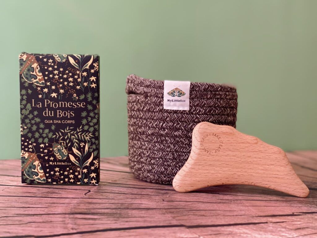 Gua sha pour le corps en bois et panière tressée de l'édition Murmures des Bois, présentés avec leur emballage illustré.
